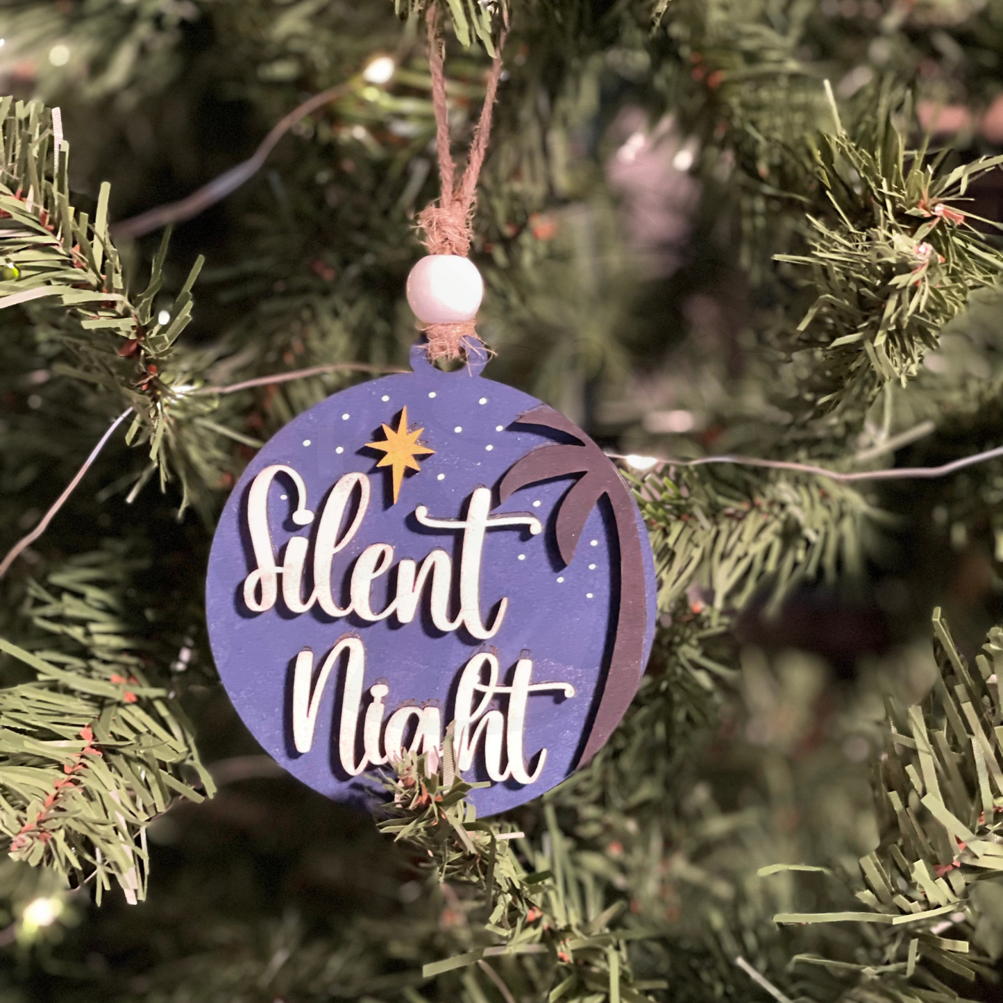 Handcrafted wood Christmas ornament with "Silent Night" design hanging on a tree.