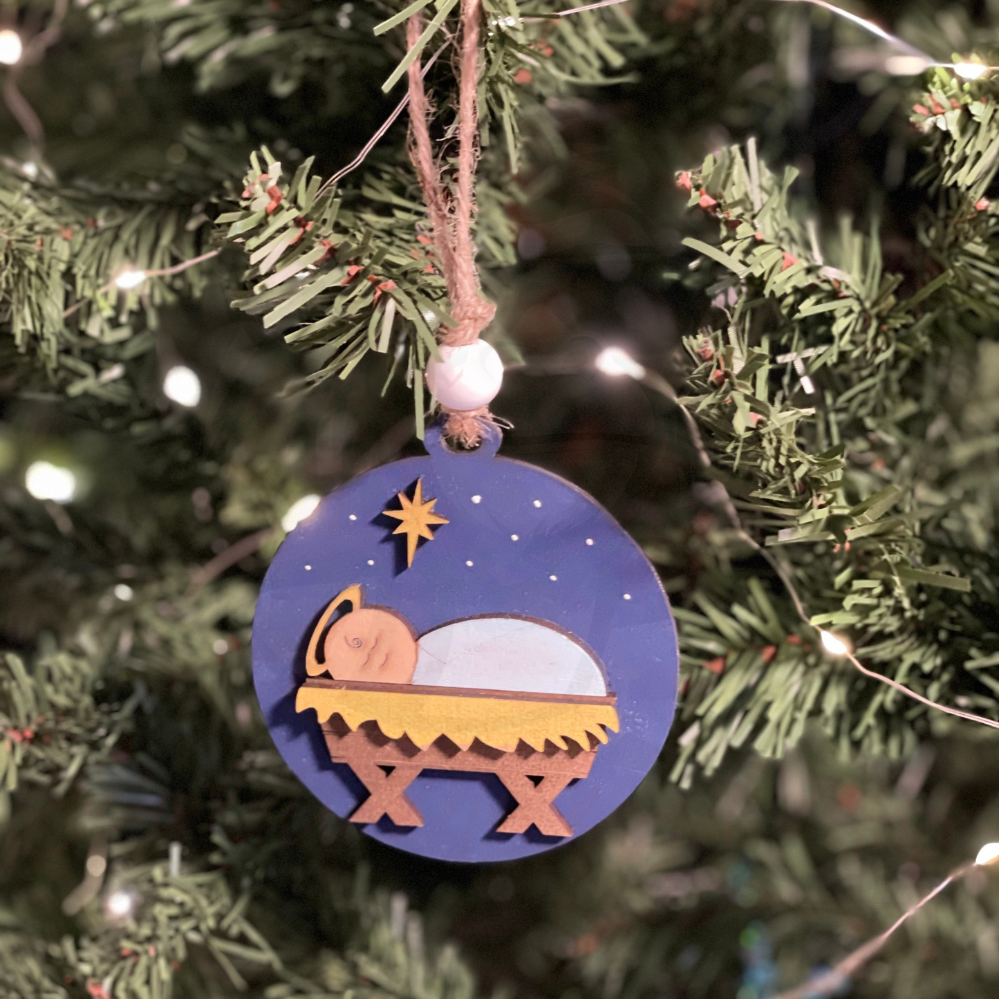 Handcrafted wooden Christmas ornament featuring a manger scene, hanging on a Christmas tree.