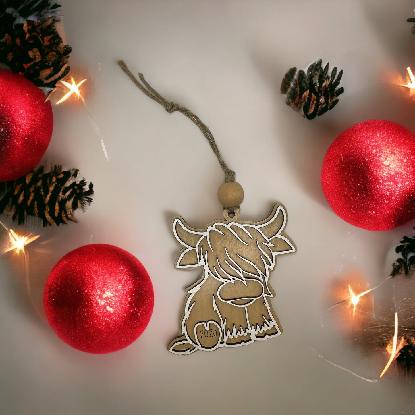 Christmas ornament featuring a Highland Cow with red baubles and lights.