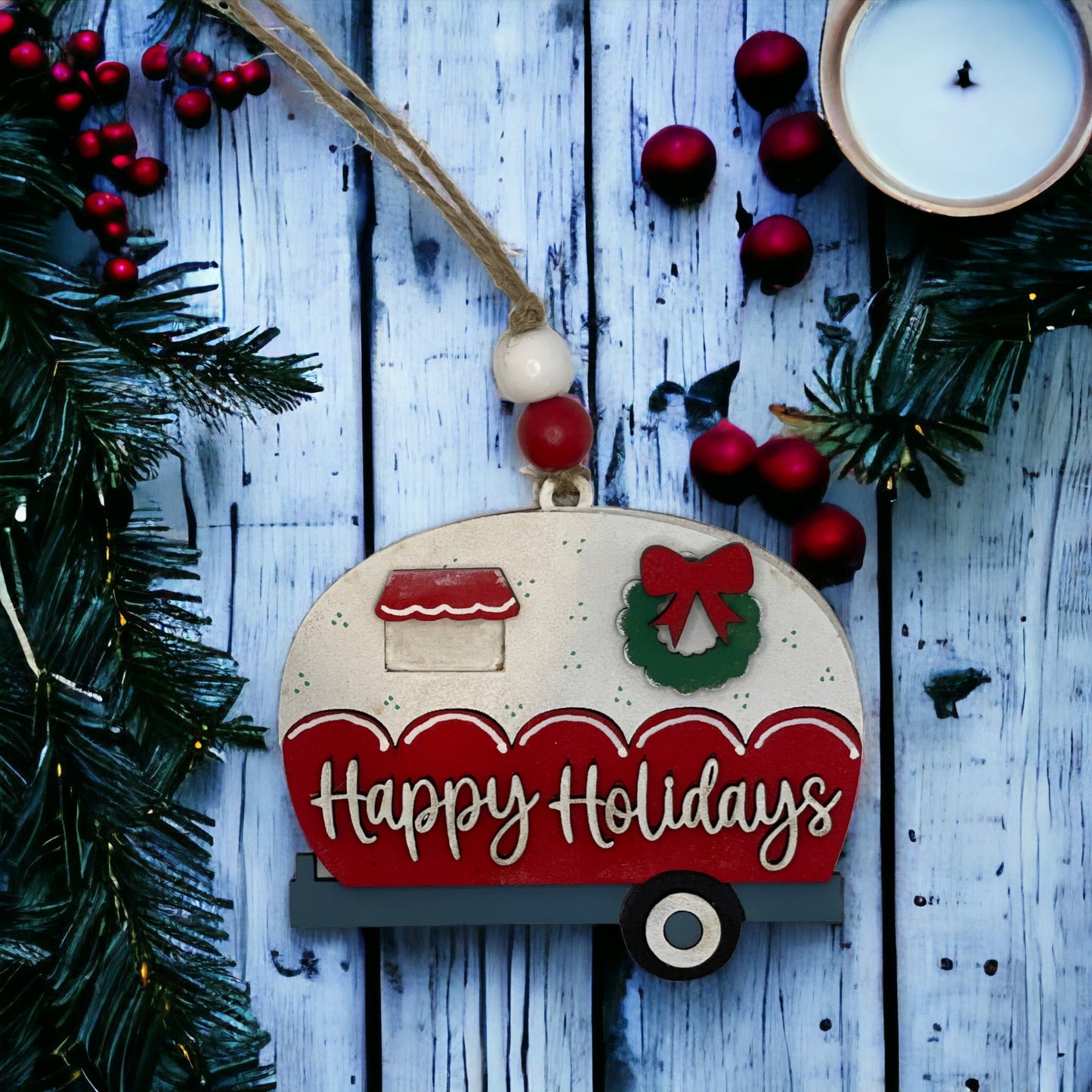 Handcrafted Christmas ornament with "Happy Holidays" camper design on rustic wood background.