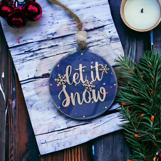 Hand-painted wooden blue "Let it Snow" Christmas ornament with hanging string on a rustic background