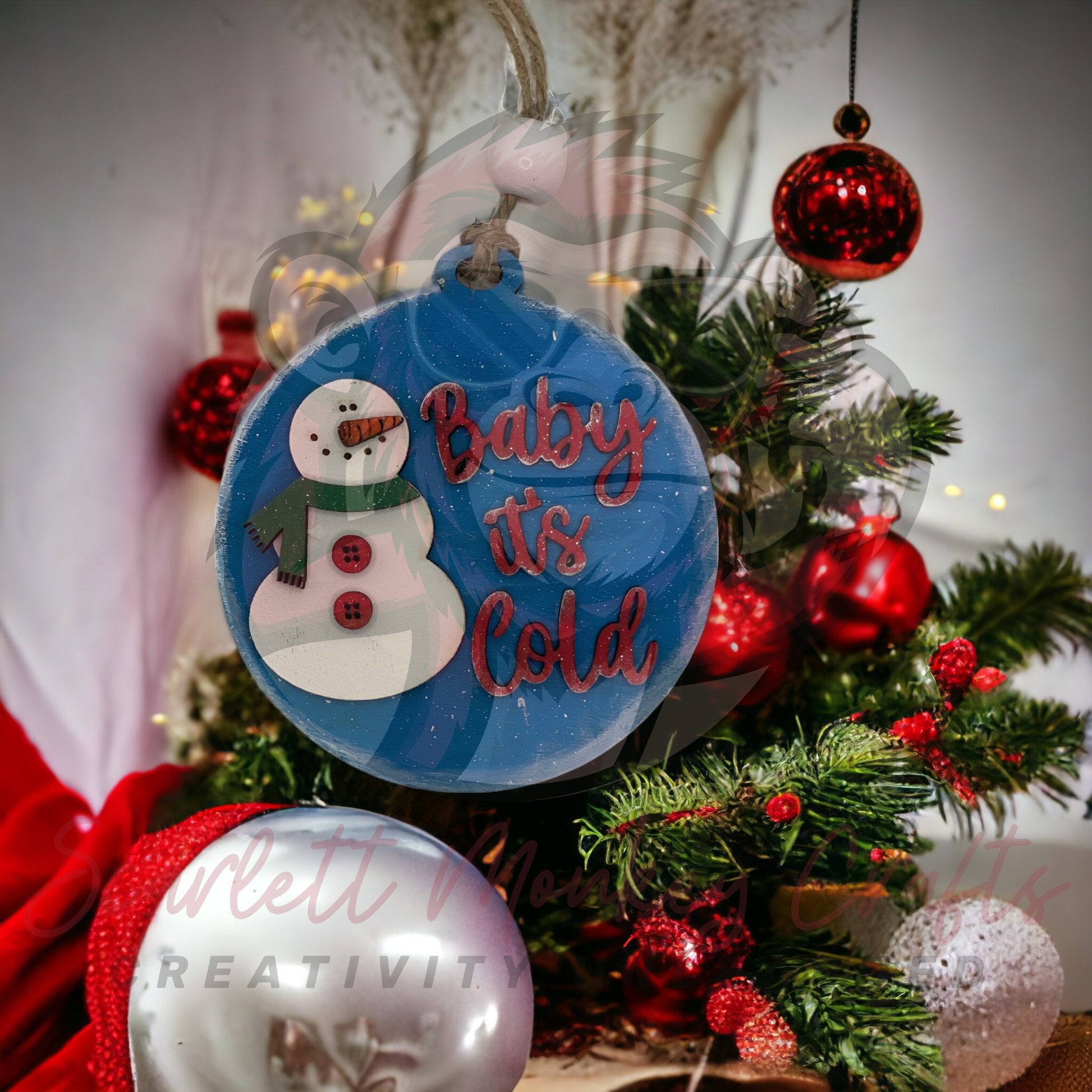 Hand-painted "Baby It's Cold" wooden Christmas ornament with snowman design hanging on festive tree
