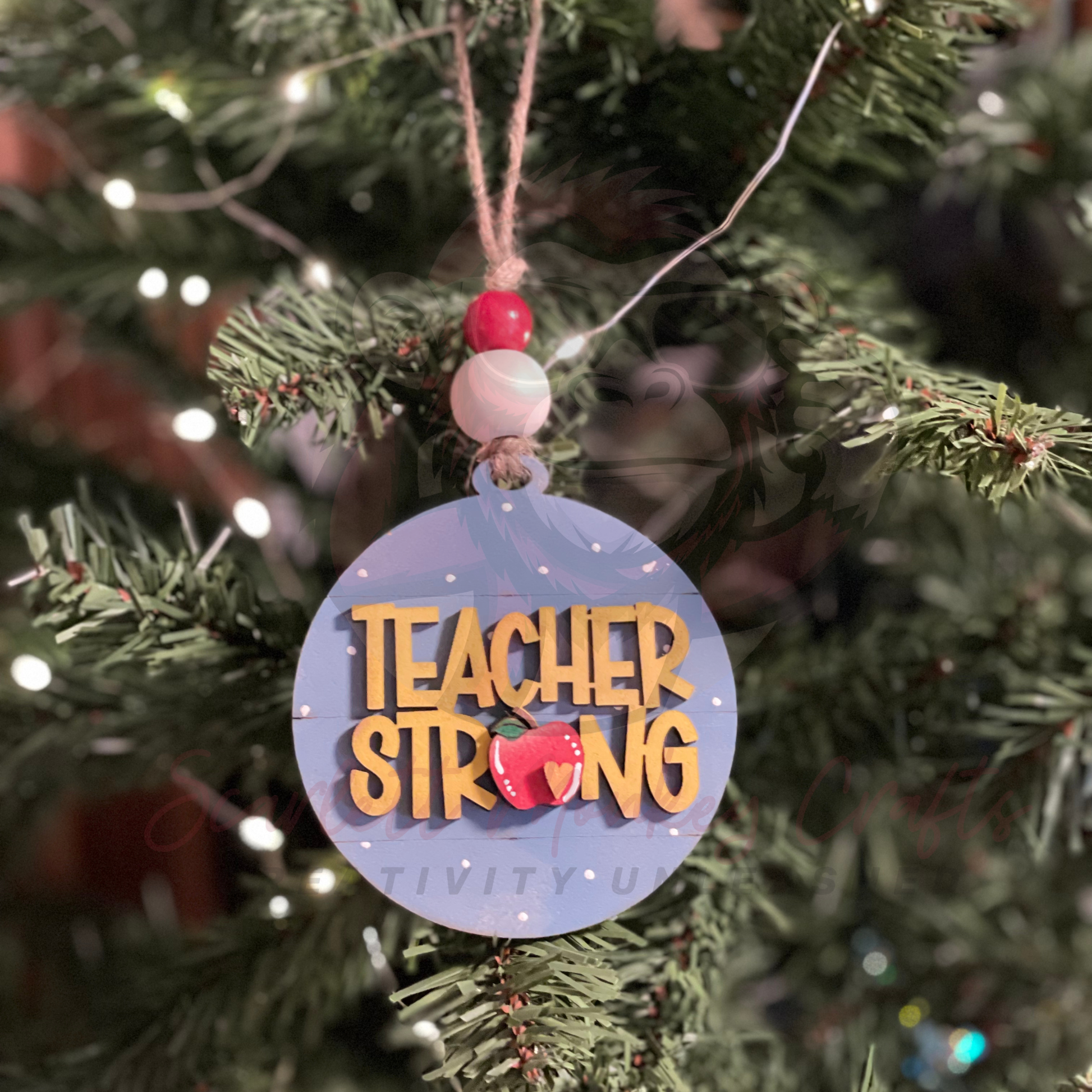 Hand-painted wooden Christmas ornament with Teacher Strong lettering and festive accents hanging on tree