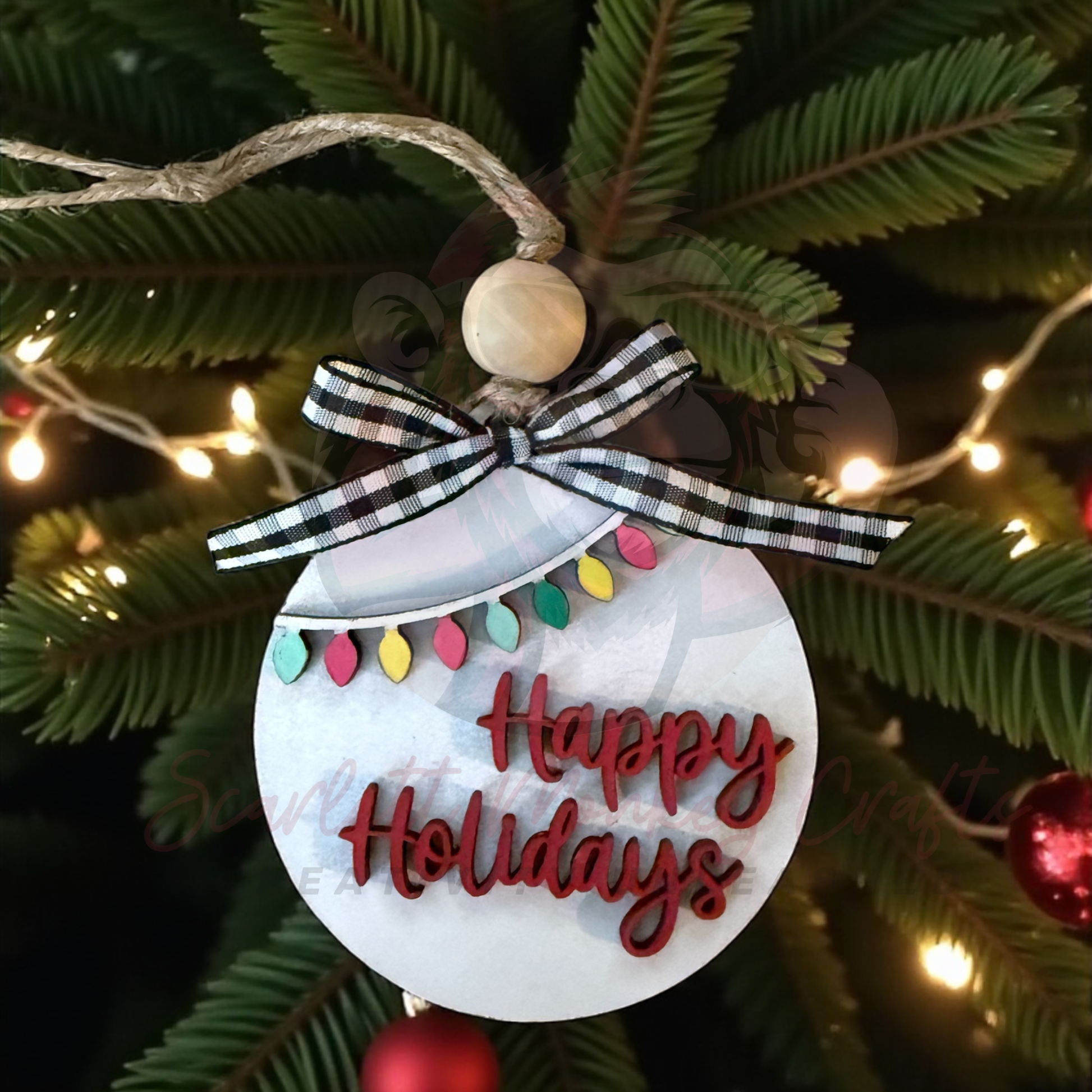 Hand-painted wooden Christmas ornament with Happy Holidays lettering and colorful lights hanging on tree with plaid bow and twine