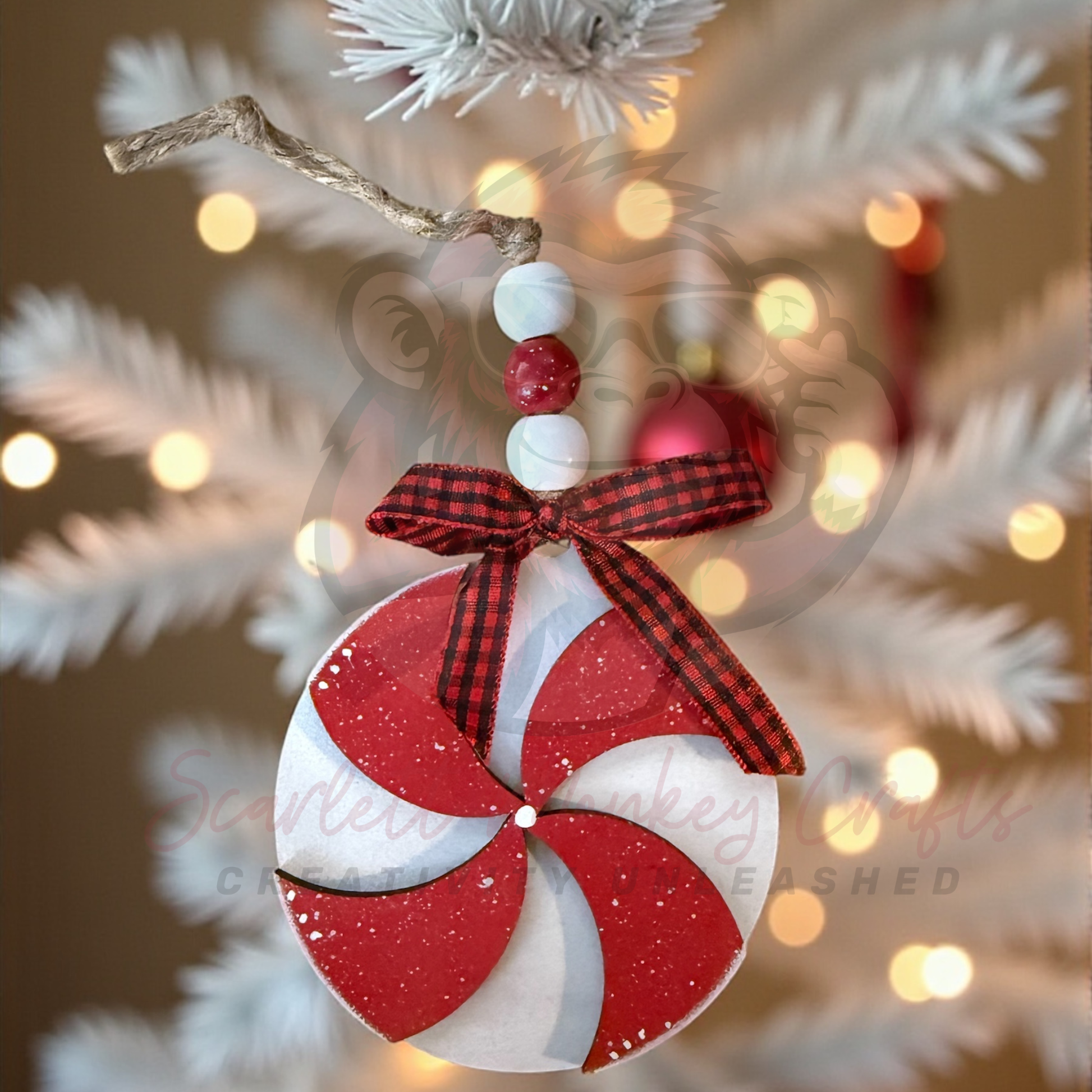 Hand-painted red and white pinwheel wooden Christmas ornament with twine hanger and plaid bow on white Christmas tree