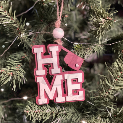Maroon and creme hand-painted Christmas ornament spelling HOME with Oklahoma as the O hanging on tree