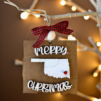 Hand-painted Oklahoma Christmas ornament with Merry Christmas lettering and red heart detail hanging on twine with plaid bow