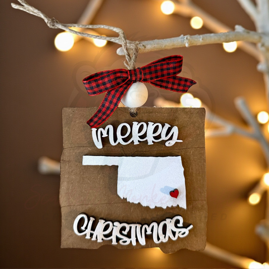 Hand-painted Oklahoma Christmas ornament with Merry Christmas lettering and red heart detail hanging on twine with plaid bow
