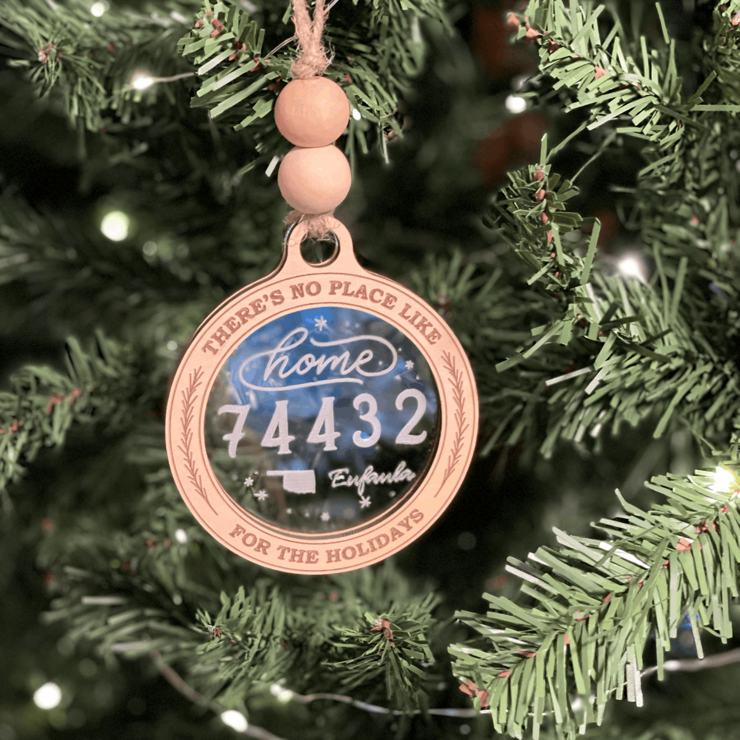 Personalized Christmas ornament with home and zip code engraving hanging on tree.