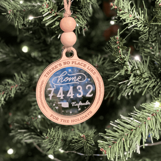 Personalized Christmas ornament with home and zip code engraving hanging on tree.
